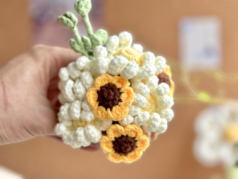 Op de afbeelding: Een gehaakt boeket van witte en gele bloemen. Het boeket bevat kleine witte bloemen en grotere gele bloemen met bruine centra.
