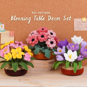 May include: A collection of three crocheted flower arrangements in brown pots. The flowers are in shades of pink, yellow, purple, and white, with green leaves. The text "Blooming Table Decor Set" is displayed above the flowers.