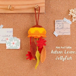 May include: A handmade crochet jellyfish mobile with autumn leaf accents. The jellyfish is yellow, orange, and brown, with red, orange, and yellow leaves hanging below. The text "Autumn Leaves Jellyfish" is visible.