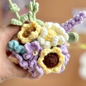 Op de afbeelding: Een gehaakt boeket bloemen in tinten geel, wit, paars en groen. Het boeket bevat zonnebloemen, madeliefjes en lavendel.