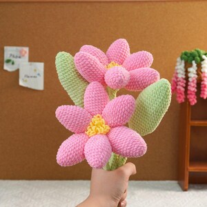 May include: A bouquet of pink crocheted flowers with green leaves. The flowers have yellow centers.
