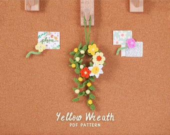 May include: A handmade crochet yellow wreath with white, orange, and yellow flowers, green leaves, and small white balls. The wreath is hanging on a corkboard. The text "Yellow Wreath PDF Pattern" is at the bottom.