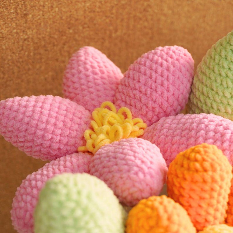 May include: A close-up of a crocheted flower bouquet with pink, green, and orange yarn. The flower has a yellow center.