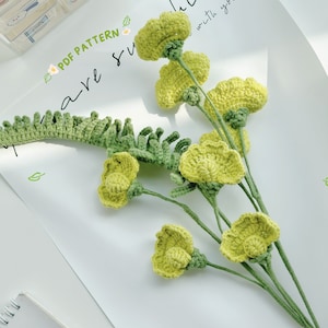 May include: A bouquet of crocheted yellow flowers with green stems and leaves. The flowers are arranged in a vase and the stems are visible. The flowers are made of yarn and the leaves are made of felt.