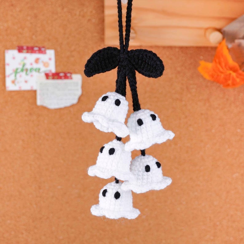 Peut inclure: D&eacute;coration d'Halloween faite &agrave; la main avec cinq fant&ocirc;mes blancs au crochet avec des yeux en points noirs, suspendus &agrave; un n&oelig;ud noir au crochet. Les fant&ocirc;mes sont suspendus &agrave; un cordon noir. L'arri&egrave;re-plan est de couleur neutre et chaude.