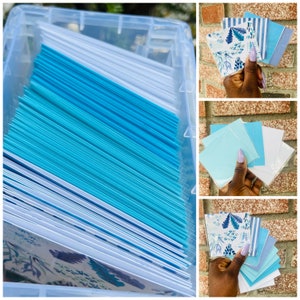 May include: A clear plastic storage box filled with a stack of blue and white greeting cards. The cards have a floral pattern and are arranged in rows. There are three smaller images showing close-ups of the cards.