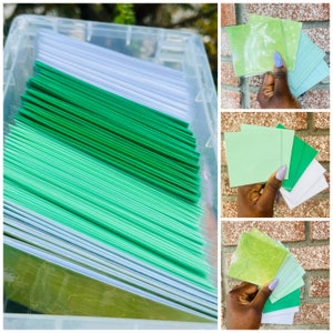 May include: A clear plastic storage box filled with stacks of green, light green, and white cardstock paper.
