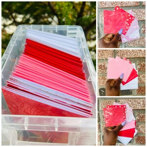 May include: A clear plastic storage container filled with a stack of red and pink greeting cards. The cards have a white border and a floral design.