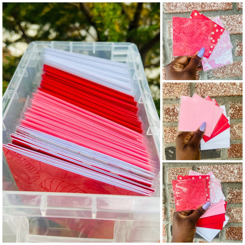 May include: A clear plastic storage container filled with a stack of red and pink greeting cards. The cards have a white border and a floral design.