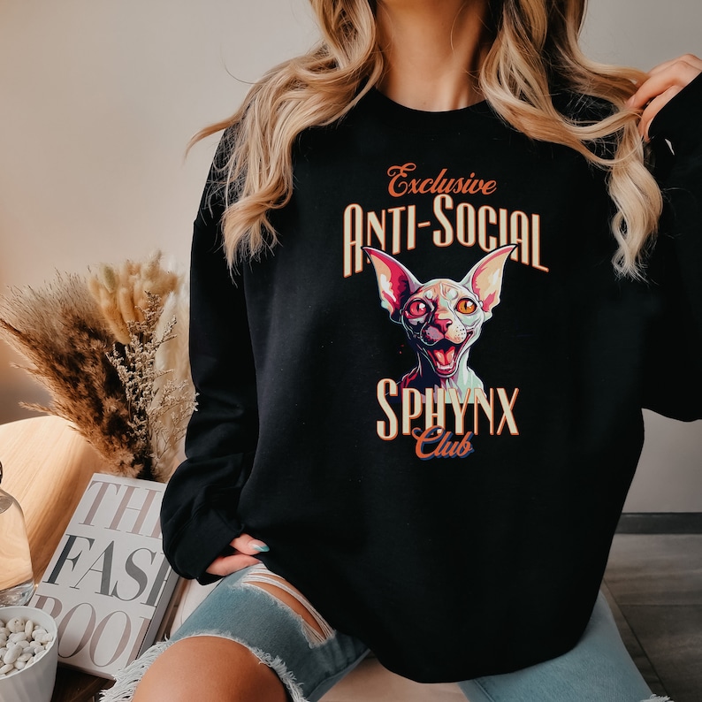 May include: Black sweatshirt with a graphic print of a white cat with orange eyes and the text "Exclusive Anti-Social Sphinx Club".