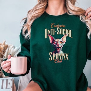 May include: Green sweatshirt with a graphic of a Sphynx cat and the text "Exclusive Anti-Social Sphynx Club".
