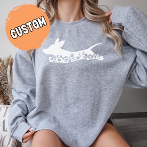 K&ouml;nnte beinhalten: Hellgraues Sweatshirt mit einem wei&szlig;en Hunde-Grafikmuster mit floralen Details. Das Wort "CUSTOM" ist wei&szlig; auf einem orangefarbenen Kreis gedruckt. Das Sweatshirt hat lange &Auml;rmel.