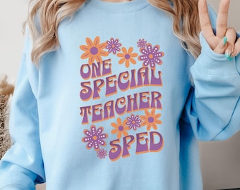 Könnte beinhalten: Hellblauer Pullover mit einer lila und orangefarbenen Grafik, auf der "One Special Teacher SPED" mit einem floralen Design steht.