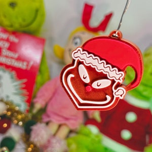 May include: A red and white Grinch ornament with a Santa hat. The ornament is made of plastic and has a shiny finish. The ornament is hanging from a string.
