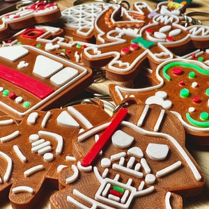 May include: A collection of gingerbread cookie keychains featuring various designs, including a snowman, a star, a gingerbread man, a Mickey Mouse head, and a Darth Vader. The keychains are brown with white and green icing details.