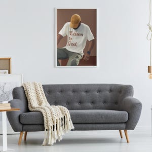 May include: A framed print of a person wearing a white t-shirt with the text "Listen to God." The person is wearing a brown baseball cap and sitting on a brown surface.
