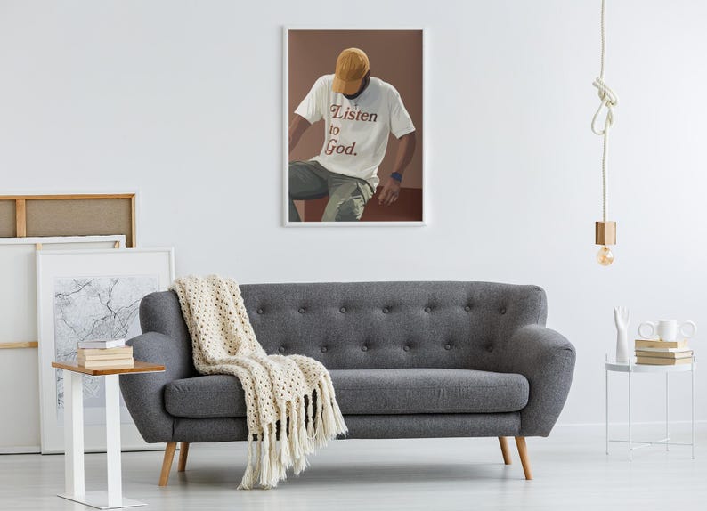 May include: A framed print of a person wearing a white t-shirt with the text "Listen to God." The person is wearing a brown baseball cap and sitting on a brown surface.