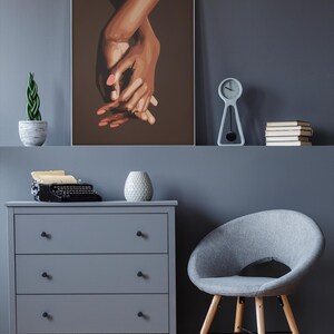 Puede incluir: Una pintura de dos manos entrelazadas, con un fondo marr&oacute;n. Las manos son marrones y tienen u&ntilde;as rosas. La pintura est&aacute; enmarcada y colgada en una pared gris.