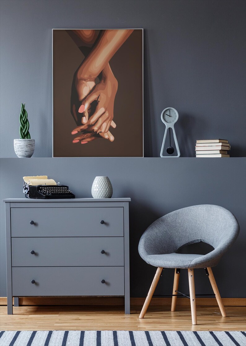 Puede incluir: Una pintura de dos manos entrelazadas, con un fondo marr&oacute;n. Las manos son marrones y tienen u&ntilde;as rosas. La pintura est&aacute; enmarcada y colgada en una pared gris.