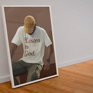 May include: A person wearing a white t-shirt with the text "Listen to God." in brown lettering. The person is wearing a brown and yellow baseball cap and khaki pants.