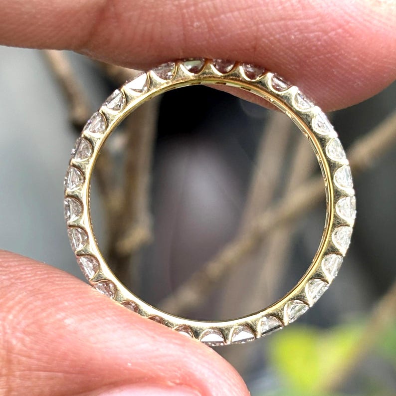 May include: A yellow gold eternity band featuring a continuous row of small, clear, round-cut gemstones set in a shared-prong setting. The ring is circular, showcasing a polished metallic finish and uniform stone placement around the entire band.