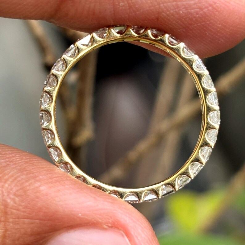 May include: A yellow gold eternity ring featuring a continuous band of small, clear, round-cut stones set in a shared-prong setting that encircles the entire circumference of the circular metal band, creating a uniform and sparkling appearance.