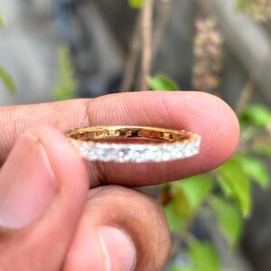 May include: A gold eternity band ring featuring a continuous row of small, clear, round-cut stones set along the outer circumference. The metal band has a polished yellow gold finish, and the stones are arranged in a shared-prong setting style.