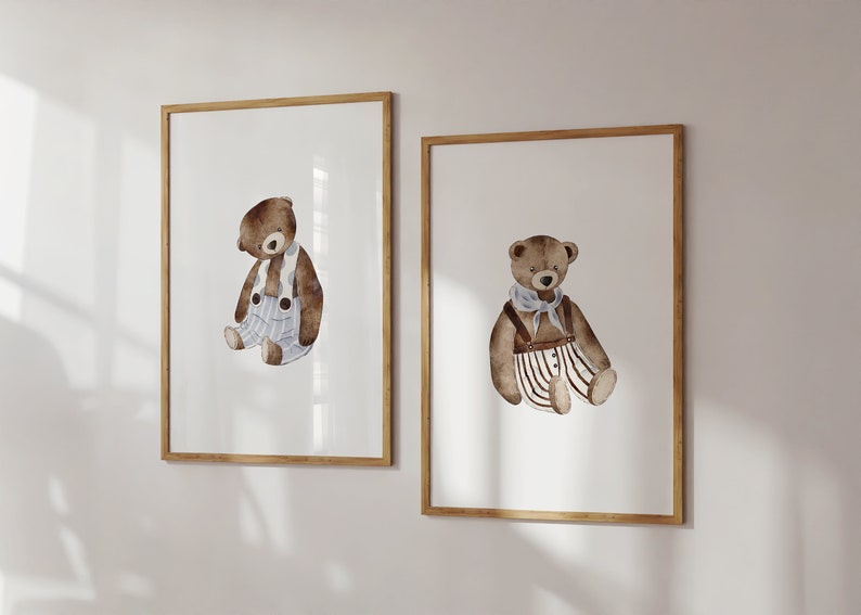 May include: Two framed prints of watercolor illustrations of teddy bears wearing overalls. The bear on the left is wearing blue and white striped overalls and a white scarf. The bear on the right is wearing brown and white striped overalls and a white scarf.