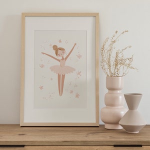 May include: A framed illustration of a ballerina in a pink tutu with a light pink background and white stars. The frame is light wood and is sitting on a wooden shelf with two pink ceramic vases.