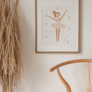 May include: A framed illustration of a ballerina in a pink tutu with a light pink background and small pink flowers. The frame is light brown wood.