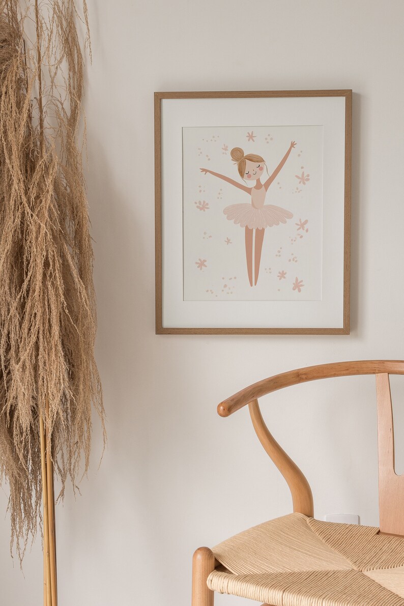May include: A framed illustration of a ballerina in a pink tutu with a light pink background and small pink flowers. The frame is light brown wood.