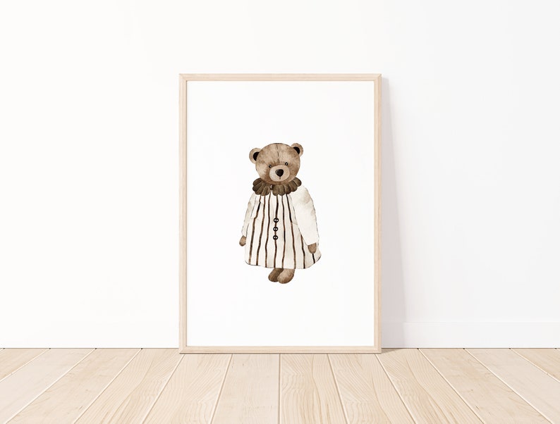 May include: A framed print of a watercolor illustration of a brown teddy bear wearing a white and black striped dress with a brown collar.