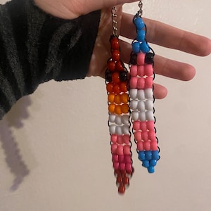 May include: Two beaded keychains. One keychain features a gradient of red, orange, and white beads. The other keychain has pink, white, blue, and black beads. Both keychains are attached to silver-colored clasps.