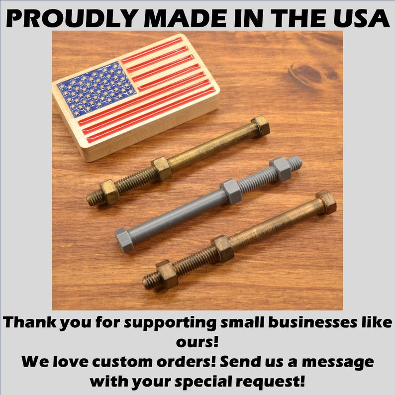 May include: Three metal bolts with nuts, two are gold and one is gray. The bolts are on a wooden surface. The image also includes a small American flag.