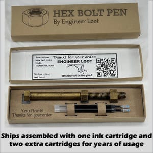 May include: A brown cardboard box with a gold metal pen shaped like a bolt. The box has the text "HEX BOLT PEN" and "By Engineer Loot" printed on it. The pen is in a smaller box inside the larger box. The smaller box has the text "You Rock! Thanks for your order" printed on it. The pen comes with two extra ink cartridges.