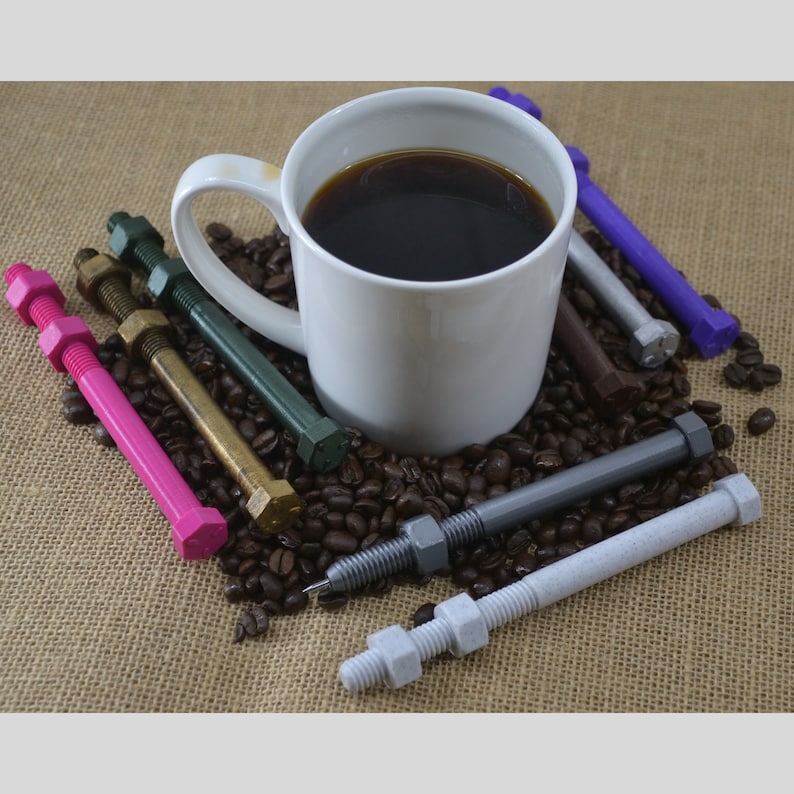 May include: A white coffee mug filled with black coffee sits on a burlap surface surrounded by coffee beans and various colored metal bolts with nuts attached.