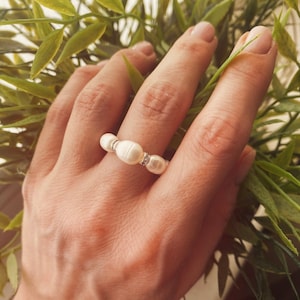 May include: A ring made of white pearls and silver. The ring is on a person's finger.