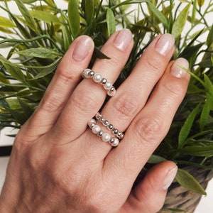 Puede incluir: Dos anillos de plata con cuentas de perlas blancas. Los anillos están apilados en un dedo.