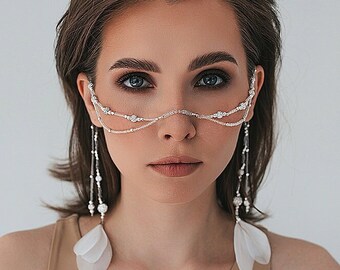 Puede incluir: Una mujer con el pelo corto y castaño que lleva un top beige sin mangas y una cadena plateada con cuentas blancas y plumas que le cuelgan de las orejas.
