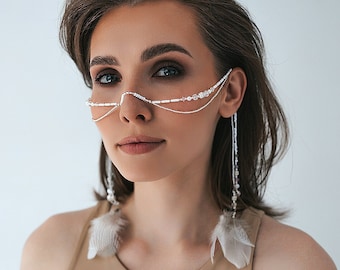 Puede incluir: Una mujer con el pelo castaño corto que lleva un top beige sin mangas y una cadena plateada con cuentas blancas y plumas que cuelgan de sus orejas.