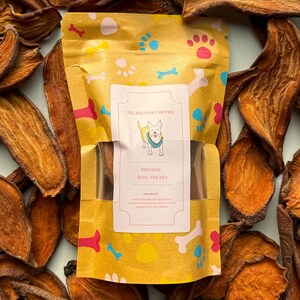 May include: A yellow bag with paw prints and bones printed on it. The bag contains homemade dog treats. The bag has a label that says "Telescope Coffee" and "Homemade Dog Treats".