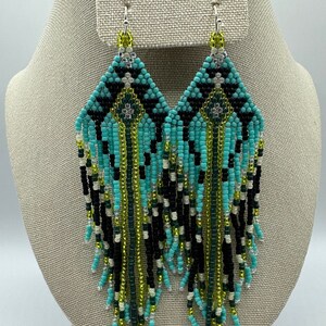 May include: A pair of turquoise, black, green, and white beaded earrings with a geometric pattern and fringe.