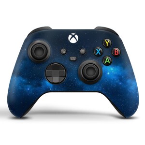 K&ouml;nnte beinhalten: Ein schwarzer Xbox-Controller mit einem blauen und wei&szlig;en Galaxie-Design. Der Controller hat ein schwarzes Steuerkreuz, schwarze Tasten und ein schwarzes Xbox-Logo.