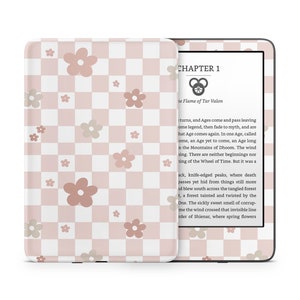 Puede incluir: Un lector electrónico Kindle Paperwhite a cuadros rosa y blanco con un patrón floral. La pantalla muestra el texto "CAPÍTULO 1" y "La Llama de Tar Valon".