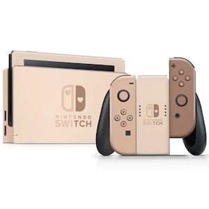 Op de afbeelding: Een lichtroze Nintendo Switch-console met een hartvormig ontwerp aan de voorkant. De console wordt getoond met twee bijpassende Joy-Con-controllers.