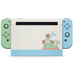 Könnte beinhalten: Eine hellblaue und grüne Nintendo Switch-Konsole mit einem benutzerdefinierten Design, das Tom Nook und andere Tierfiguren aus der Animal Crossing-Videospielserie zeigt. Die Konsole hat einen weißen Hintergrund mit einem blauen Meer und einer grünen Insel mit Palmen.