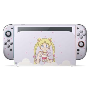 Può includere: Una console Nintendo Switch bianca con una skin personalizzata raffigurante un personaggio anime che mangia da una tazza. Il personaggio ha i capelli biondi ed è circondato da cuori rosa. I Joy-Con sono bianchi con dettagli rosa.
