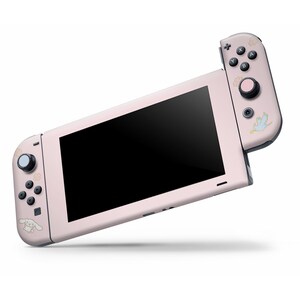 May include: A pink Nintendo Switch console with a custom design featuring a cartoon dog and a bird. The console is in handheld mode with the Joy-Con controllers attached.