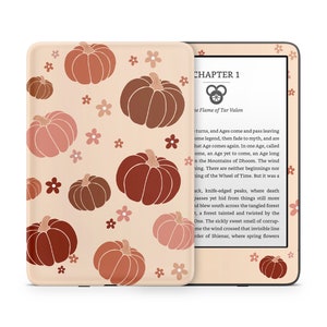 May include: A Kindle e-reader with a peach-colored case featuring a pattern of brown and pink pumpkins and small white flowers. The screen displays the text "CHAPTER 1" and "The Flame of Tar Valon".