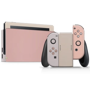 May include: A pink and beige Nintendo Switch console with two controllers. The console is in a closed position and the controllers are attached to the sides.